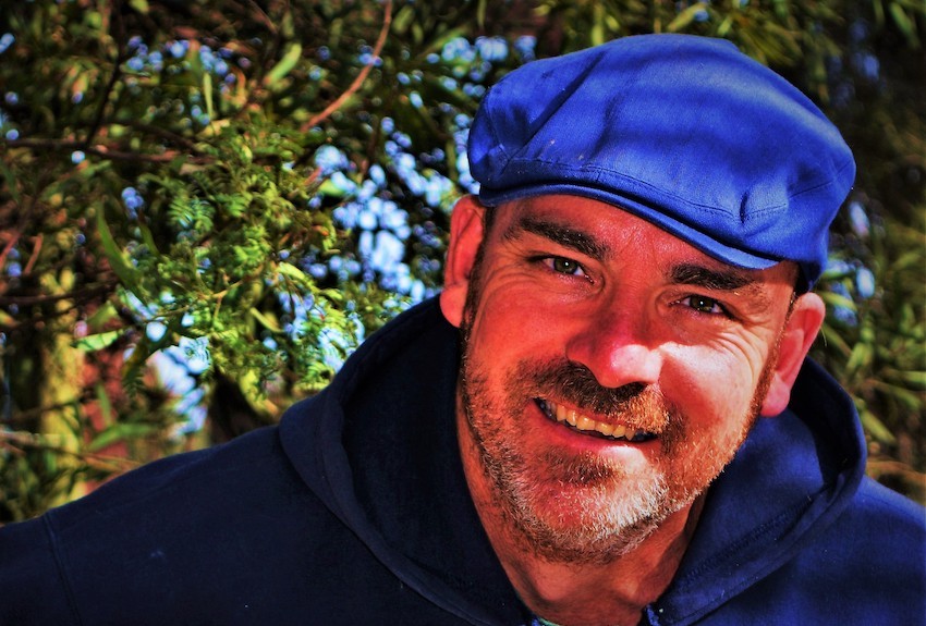 Bede wearing blue hat and smiling with trees in the background