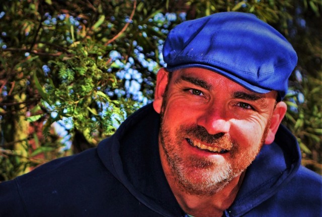 Bede wearing blue hat and smiling with trees in the background