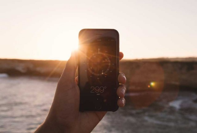 Hand is holding a phone with a compass on it held up in front of setting sun