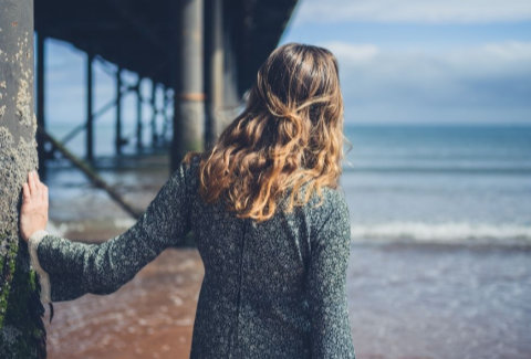 Woman standing next to a pier looking out at the ocean