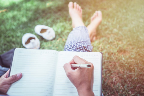 A woman sitting on grass writing in her diary