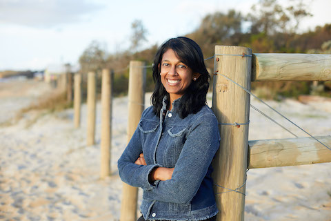 person smiling at camera leaning against wooden fence at the beach