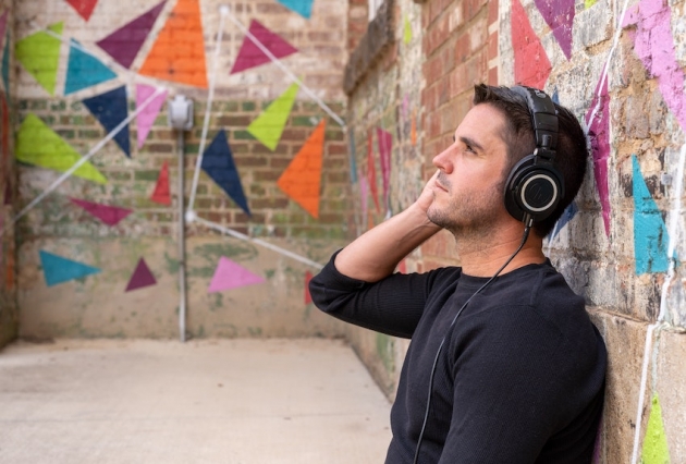 Person wearing headphones is leaning against a wall looking at the sky